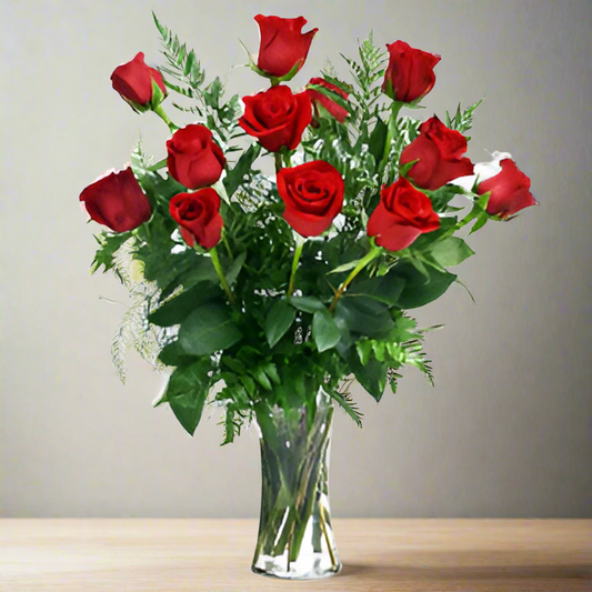 A dozen long stem red roses with foliage, arranged in a clear glass vase.