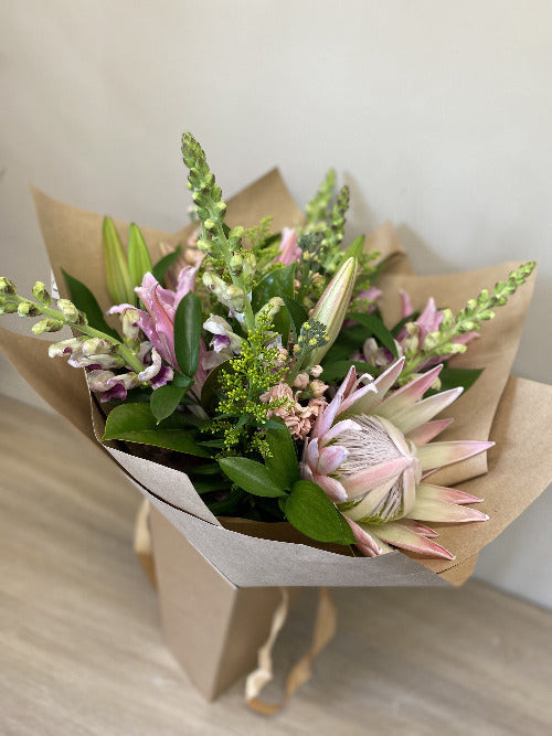 An elegant bouquet of blush pink flowers with green foliage, wrapped in a natural brown paper wrap