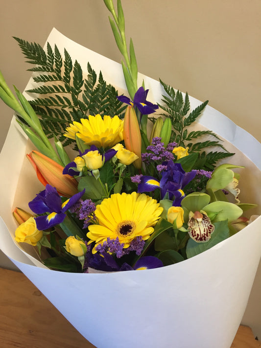 Tropical floral colours including yellow, purple, and orange flowers with green foliage, wrapped in white paper